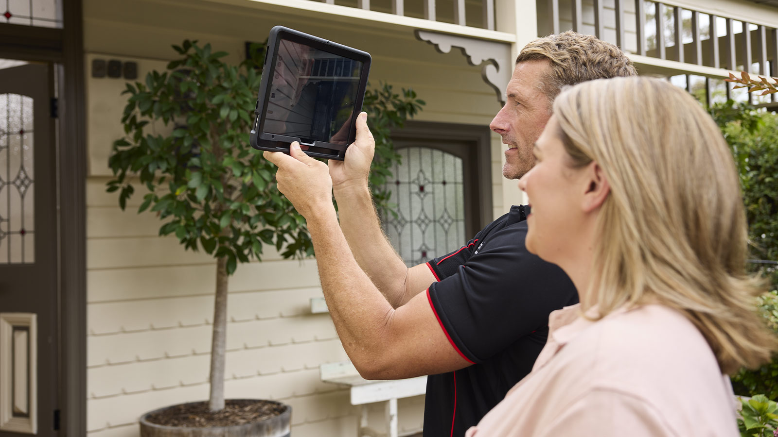 Building inspector taking photos of the exterior of a house, with the customer.