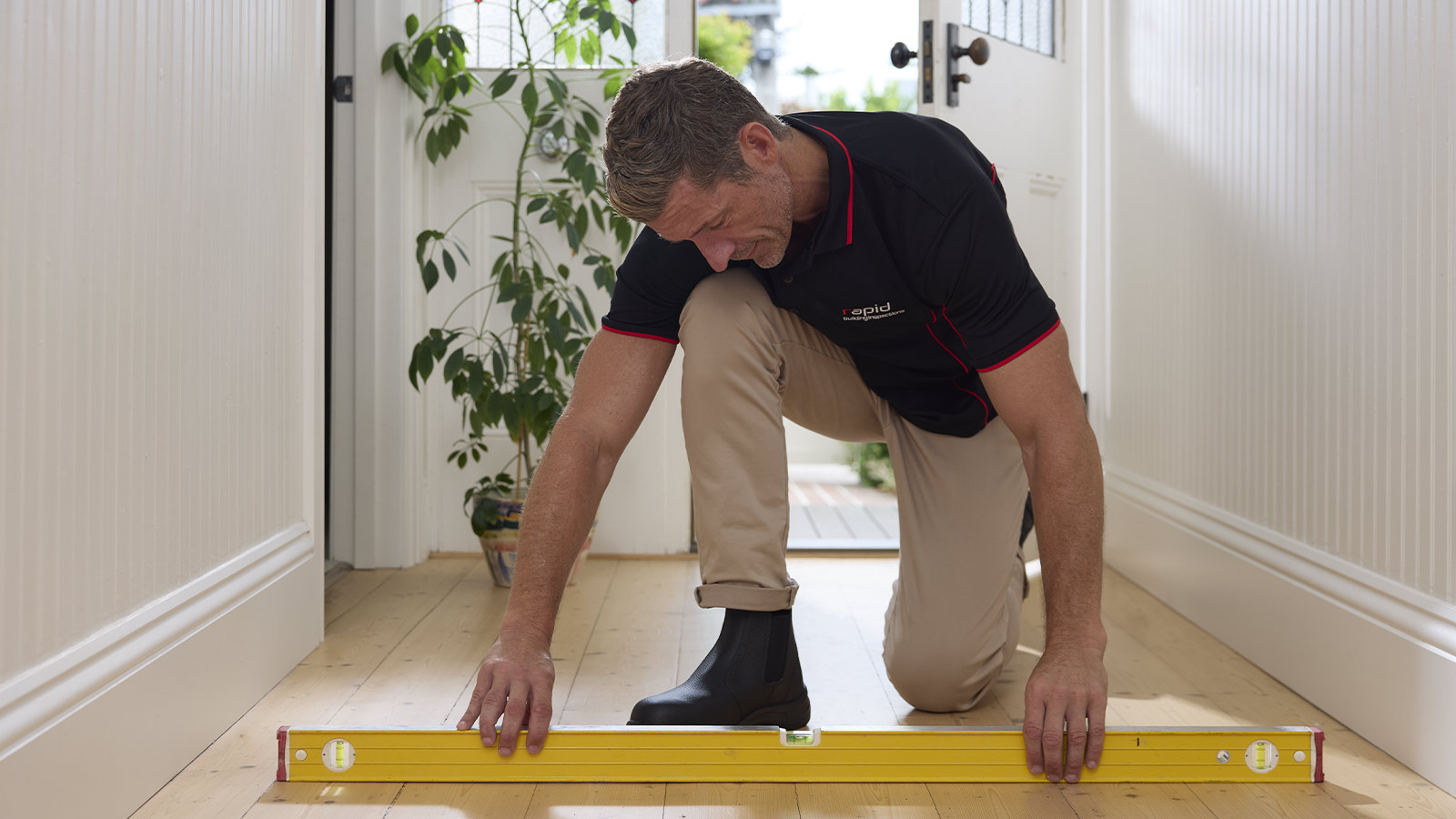 Building inspector kneeling down using a level to examine the floor.