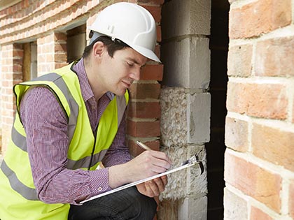 Building inspector in high-vis vest and hard hat taking notes on clipboard.