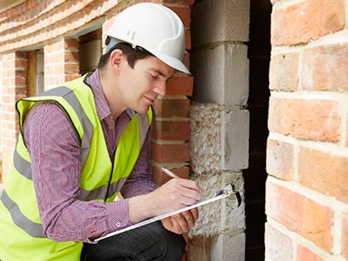 Building inspector in high-vis vest and hard hat taking notes on clipboard.