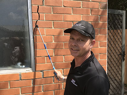 Building inspector indicating towards a cracked, brick wall.