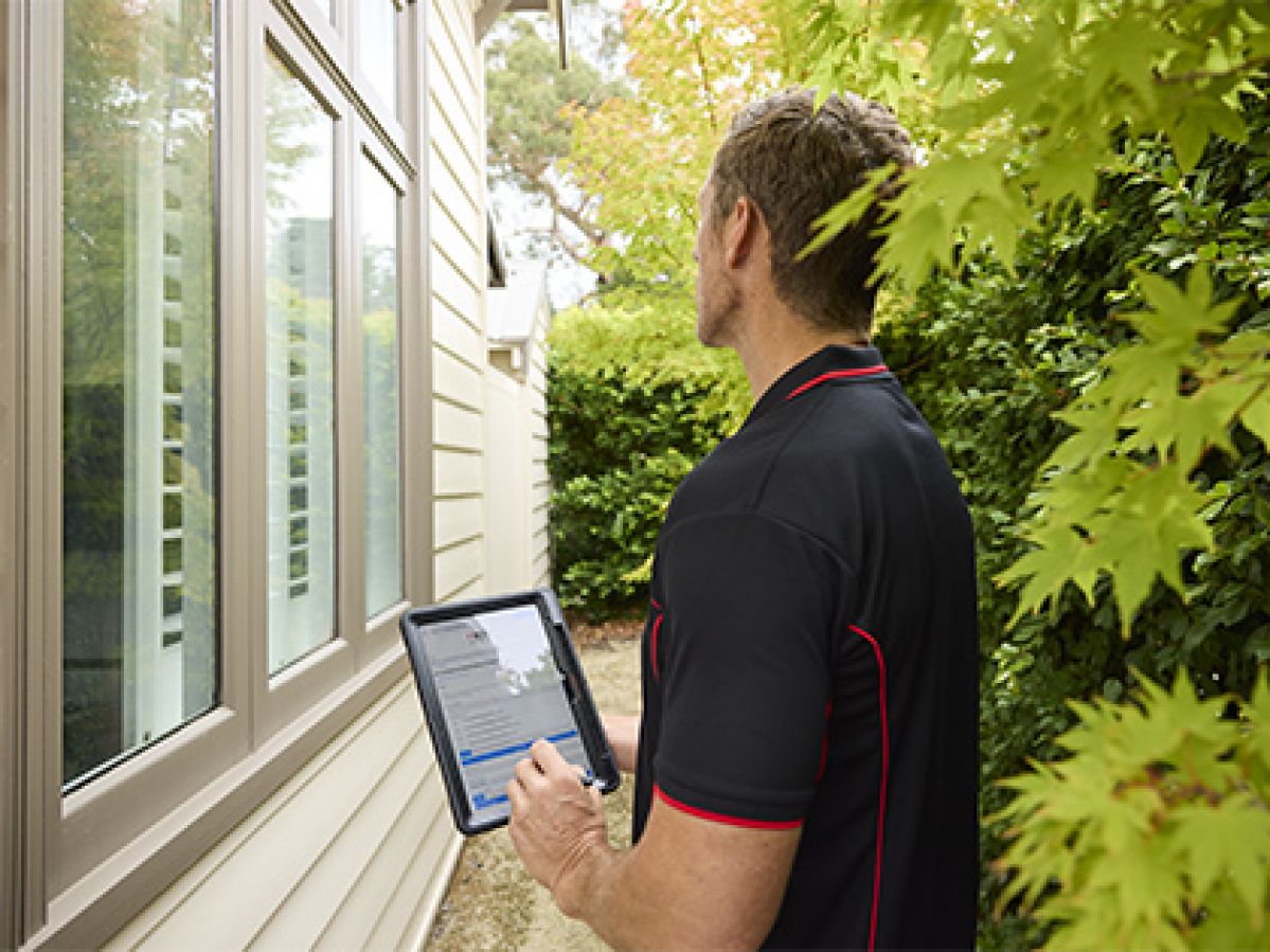 Building inspector observing the exterior of a house, while using an iPad.