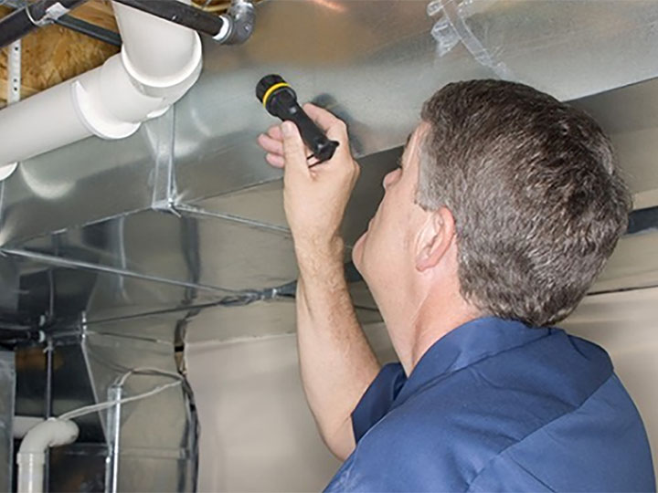 Building inspector looking at ceiling pipes and insulation with a torch.