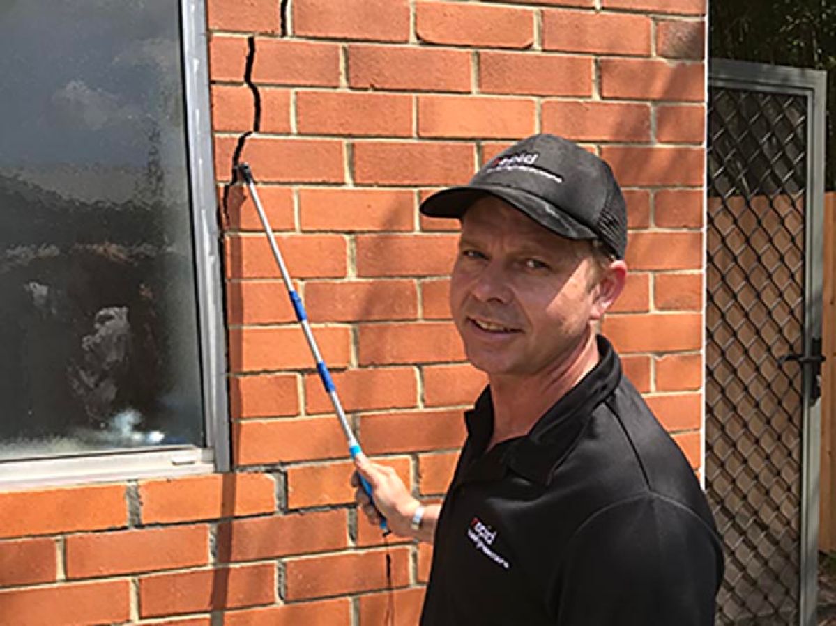 Building inspector indicating towards a cracked, brick wall.
