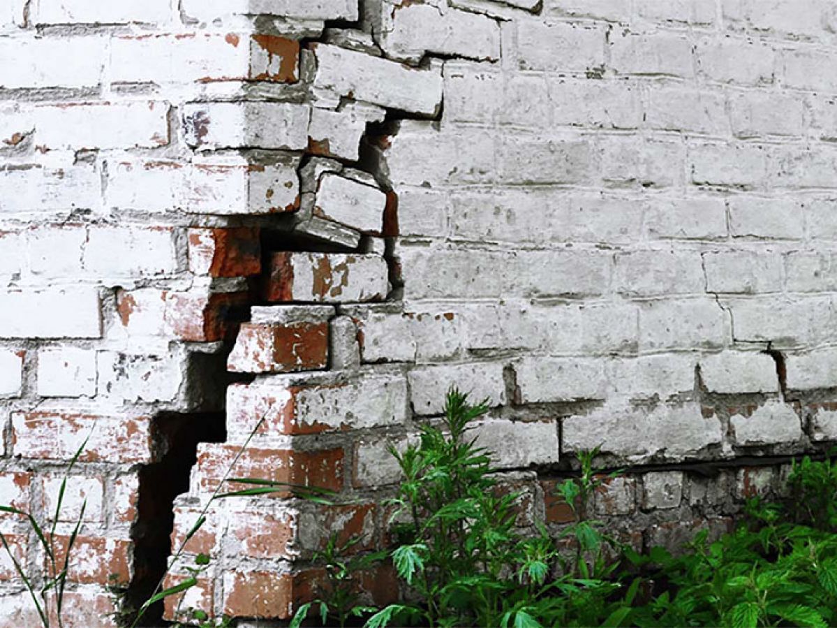 Corner shot of cracked brick wall, painted white.