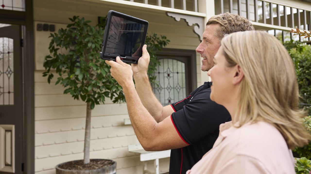 Building inspector taking photos of the exterior of a house, with the customer.
