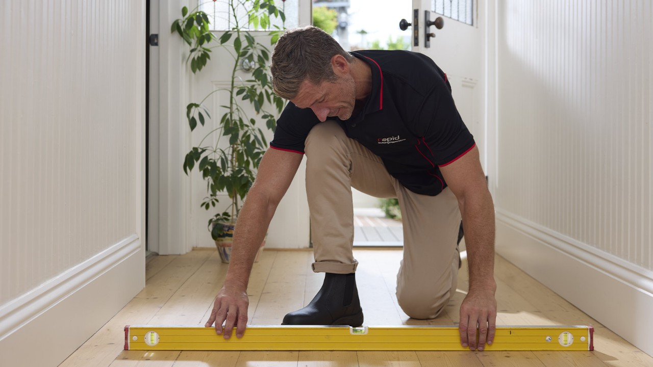 Building inspector kneeling down using a level to examine the floor.