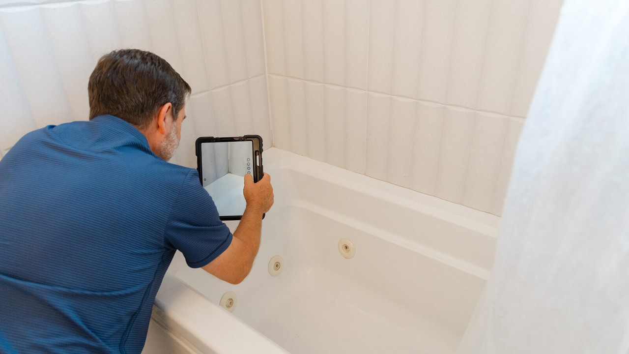 Inspector taking photos of a shower-over-bath using a tablet.