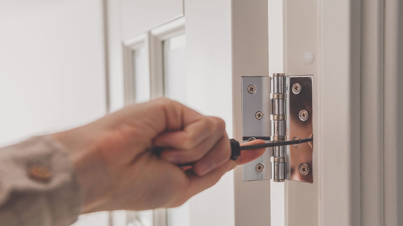 door-hinge-1600x900.jpg Close up image of man's hand screwing in a door hinge.