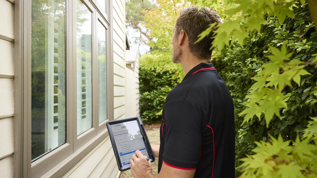Building inspector observing the exterior of a house, while using an iPad.